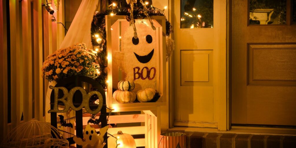 A festive Halloween porch decoration with a light-up 'BOO' sign, pumpkins, and string lights.