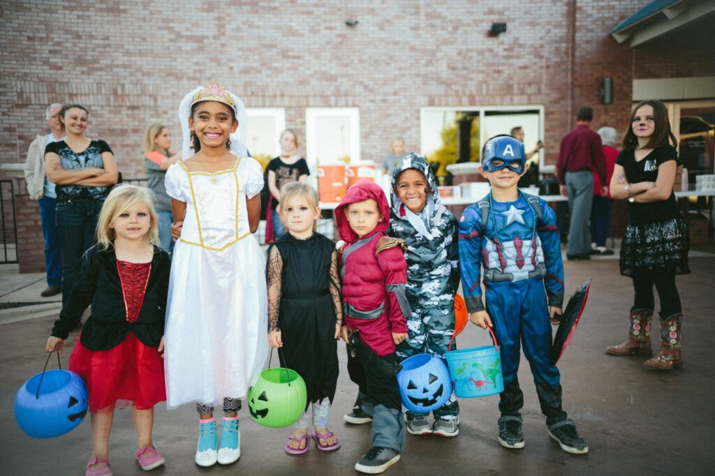 A group of children in various Halloween costumes, including a princess and a superhero, happily trick-or-treating.