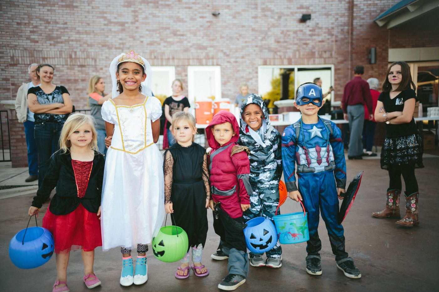 A group of children in various Halloween costumes, including a princess and a superhero, happily trick-or-treating.