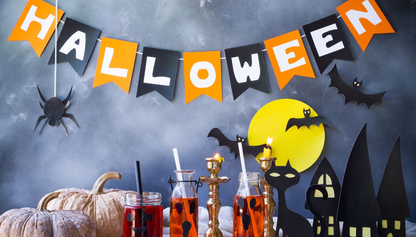 A festive Halloween party setup with a 'HALLOWEEN' banner, spooky drinks, and bat decorations.