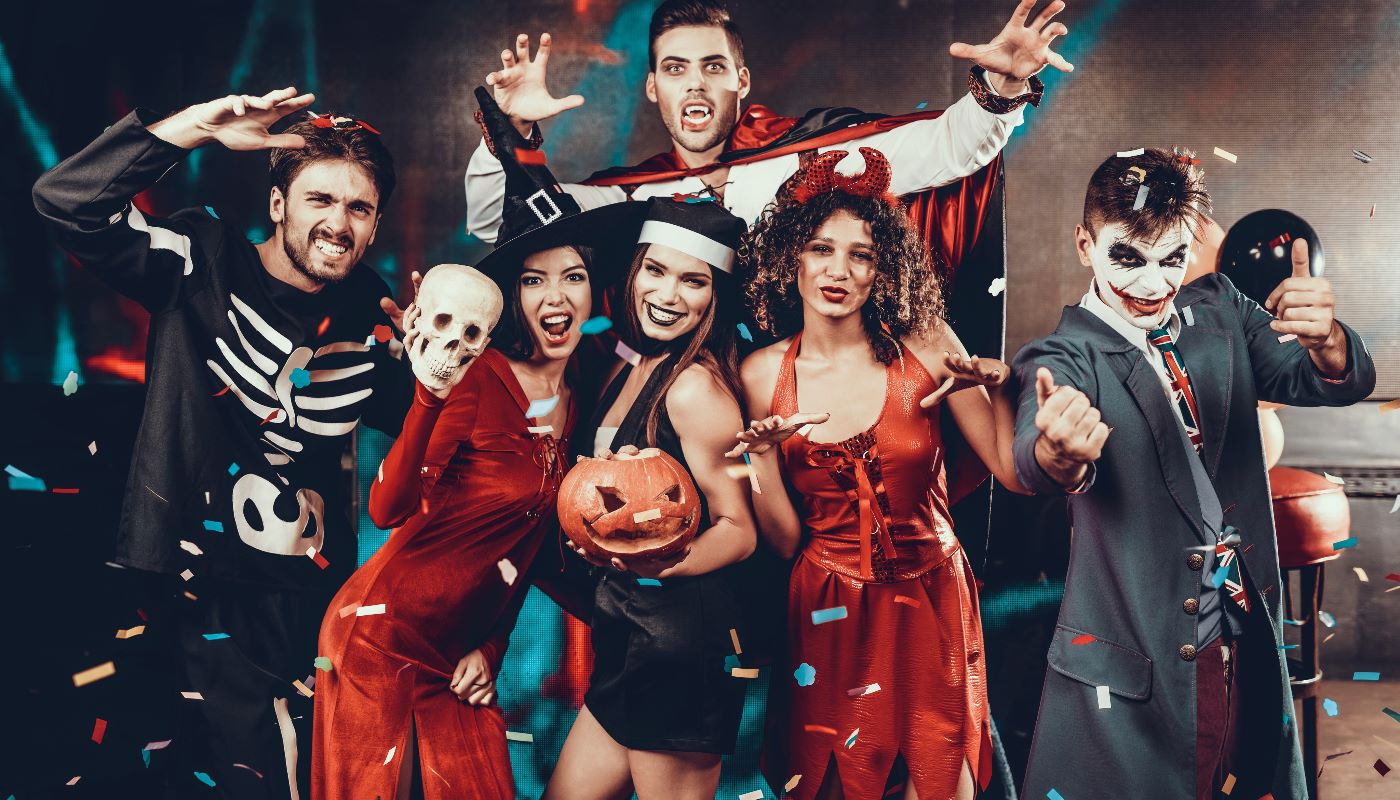 A group of friends in elaborate Halloween costumes, including Dracula and witches, posing for a photo at a party.