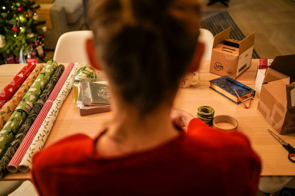 A view from over the shoulder of a person wrapping Christmas gifts at a desk.