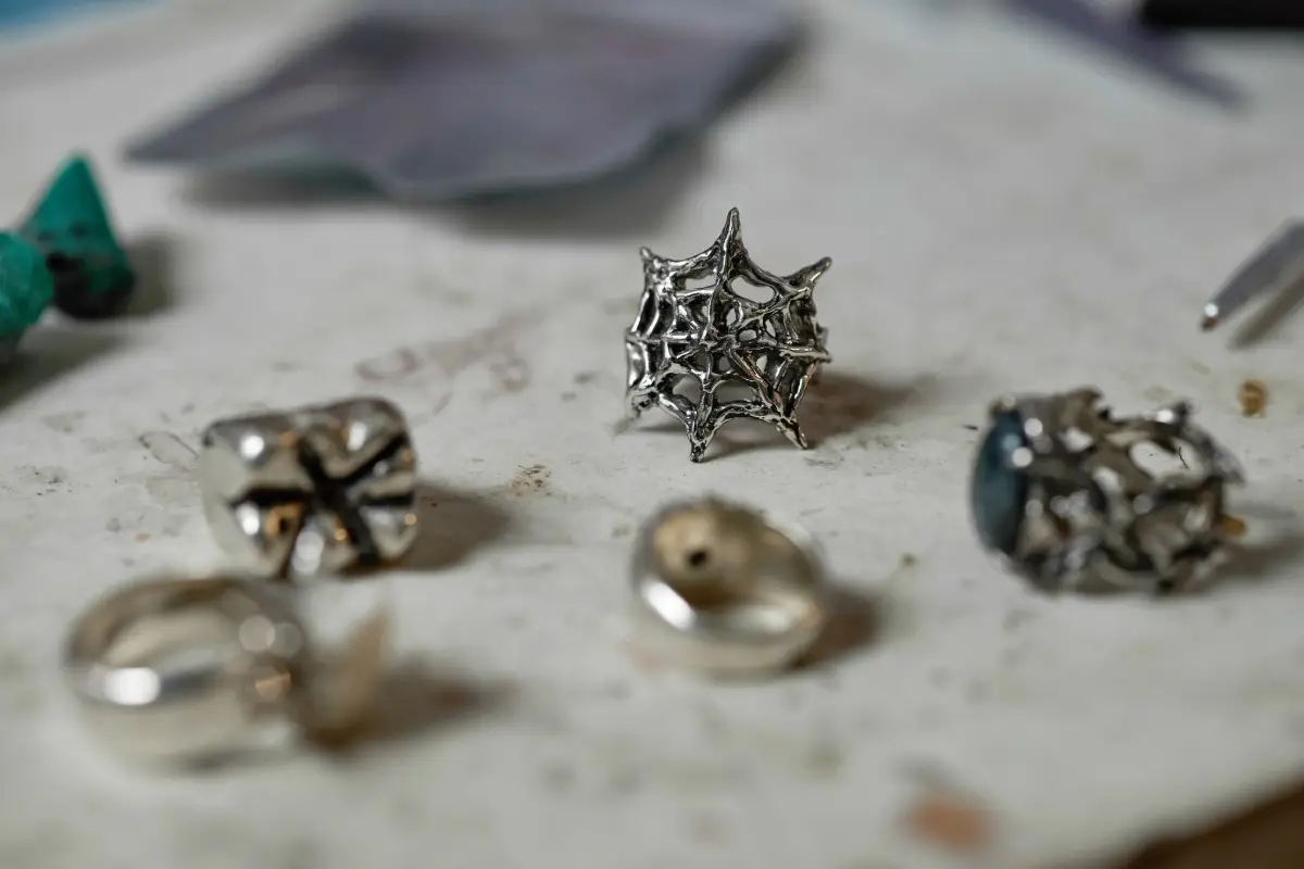A macro shot of an intricate, silver-colored spiderweb stud earring, a perfect example of a subtle but spooky piece of Halloween jewelry.