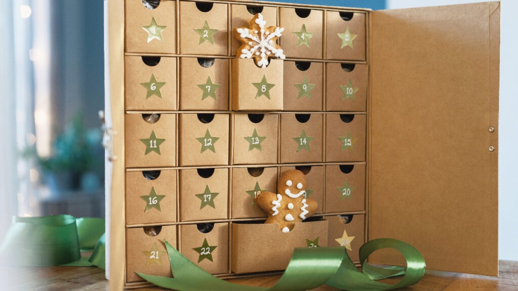 A rustic DIY advent calendar made of small craft paper drawers with stars, decorated with a gingerbread man cookie.