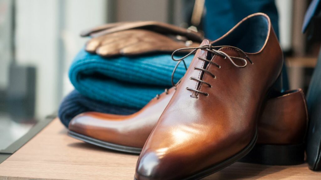 A classic men's fashion flat lay featuring a pair of polished brown leather dress shoes and a folded blue sweater.