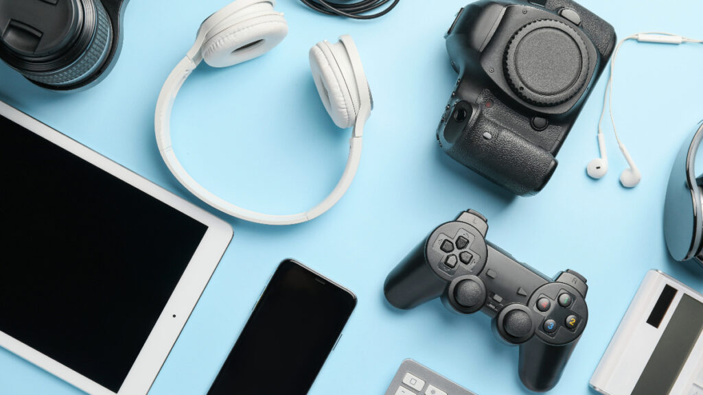 A flat lay of various electronic gadgets on a blue background, including headphones, a camera, and a gaming controller.