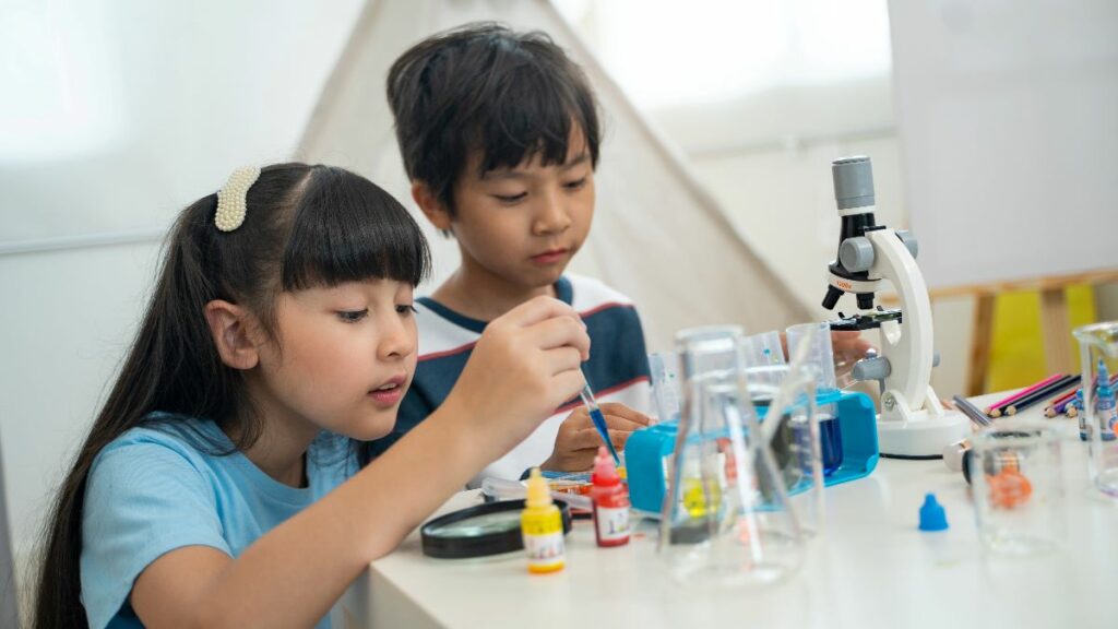 Two young children engaged in a fun science experiment, using a microscope and colorful liquids in beakers, playing with biological educational toys for kids.