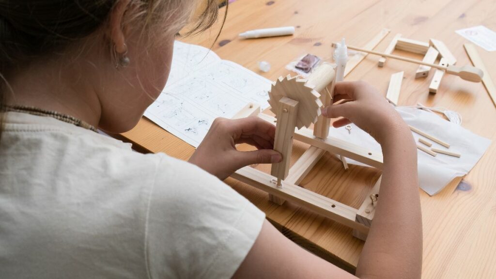 A child's hands carefully assembling a small wooden mechanical model, a STEM craft project, creative educational toys for kids.