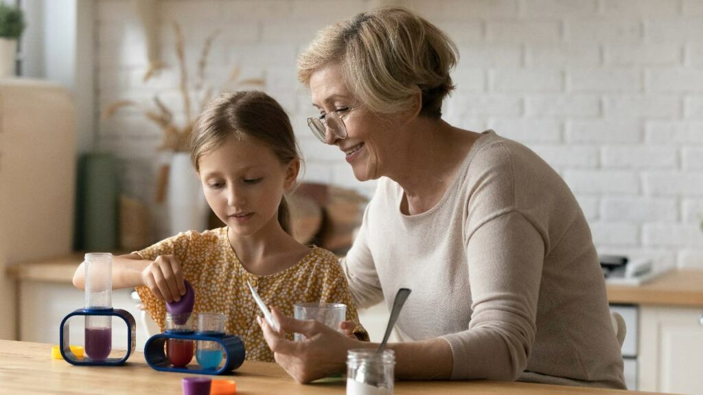 A smiling grandmother and her granddaughter playing with experimental educational toys together at a wooden table.