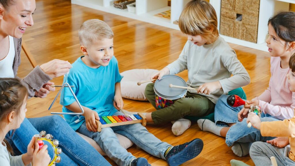 Children sitting on the floor and making music together with a small drum and a colorful xylophone.