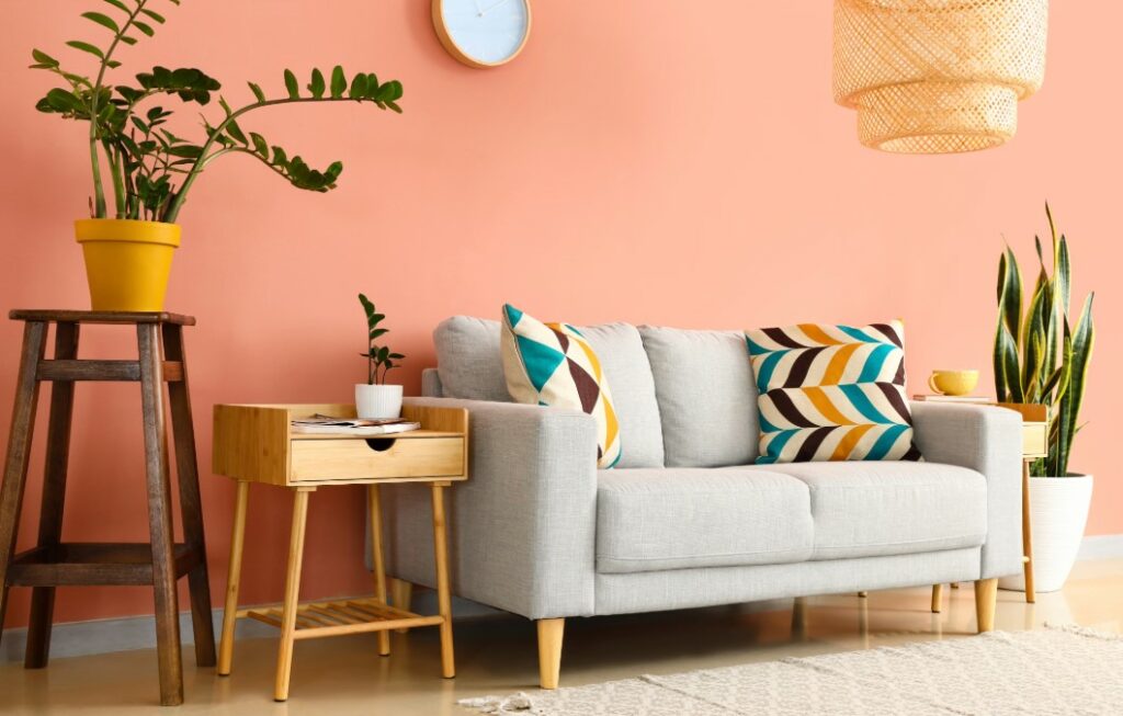 A comfortable living room with a light grey sofa and colorful pillows, set against a warm peach-colored wall.