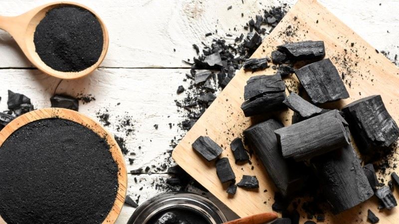An overhead view of activated charcoal pieces and powder on a white wooden surface, a natural ingredient used for purification and deodorizing.