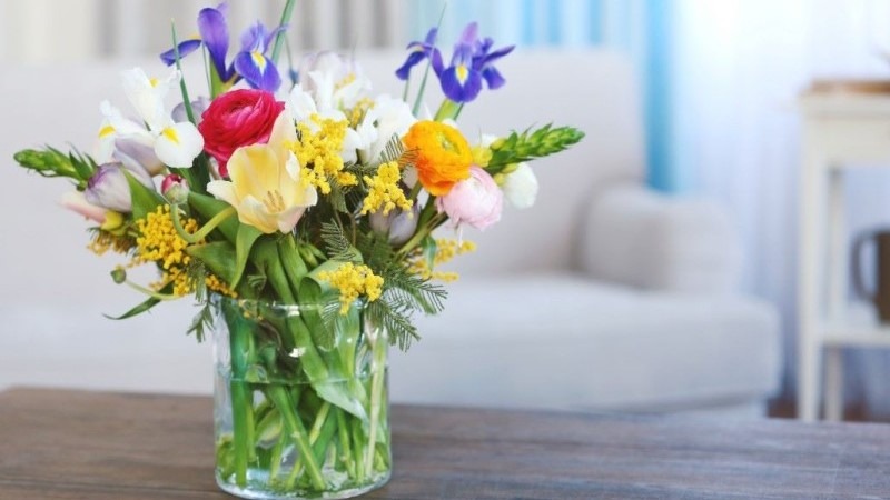 A beautiful bouquet of fresh, colorful spring flowers in a clear glass vase sitting on a wooden table, brightening the home.