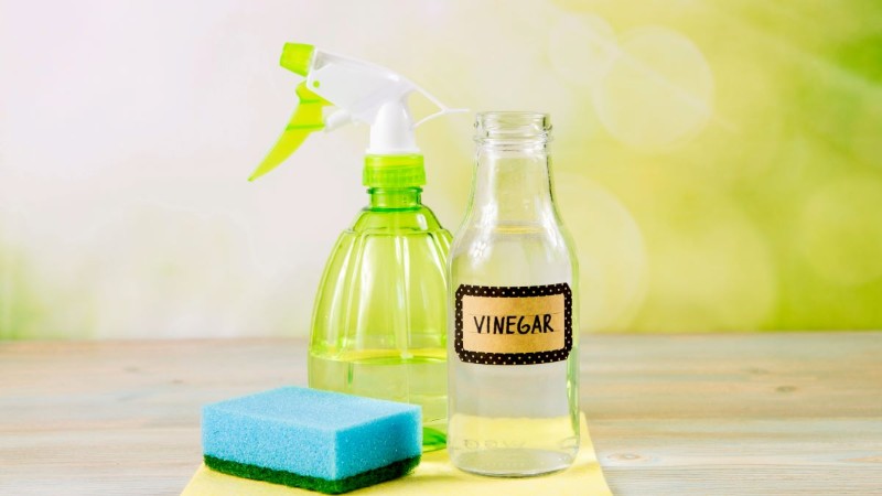 A bottle of white vinegar next to a spray bottle, representing a natural cleaning solution to eliminate odors and make your home smell fresh.