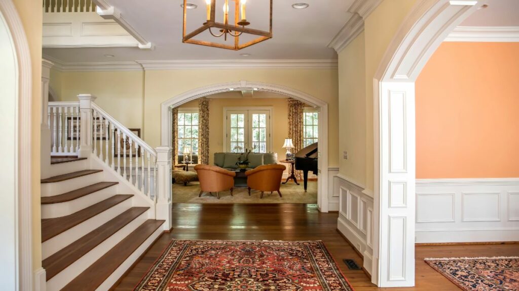 The elegant foyer of a traditional home, with an archway leading into a living room, a staircase, and an oriental rug.