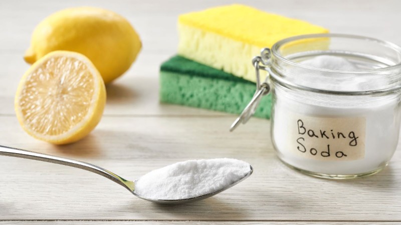 Natural cleaning supplies, including baking soda on a spoon and a fresh lemon, used as a powerful deodorizer to help make your home smell amazing.