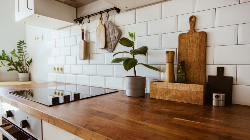 A clean and modern kitchen with a warm wooden countertop, white subway tile backsplash, and a small potted plant.