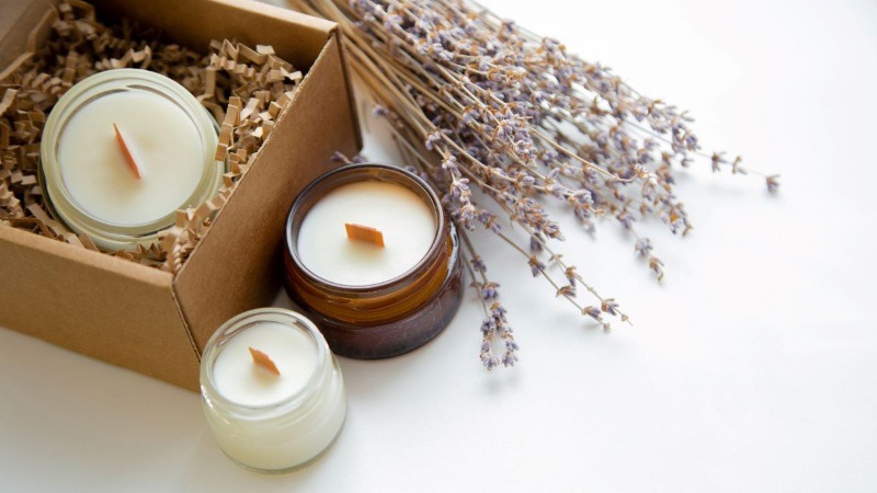 Three handmade candles with wooden wicks presented in a gift box with a bundle of dried lavender, making a thoughtful gift.