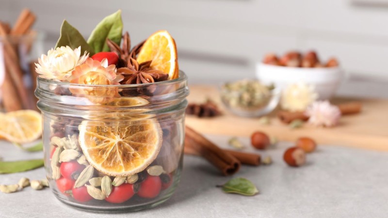 A glass jar filled with natural potpourri ingredients like dried orange slices, cinnamon sticks, and star anise for a DIY way to make your home smell amazing.