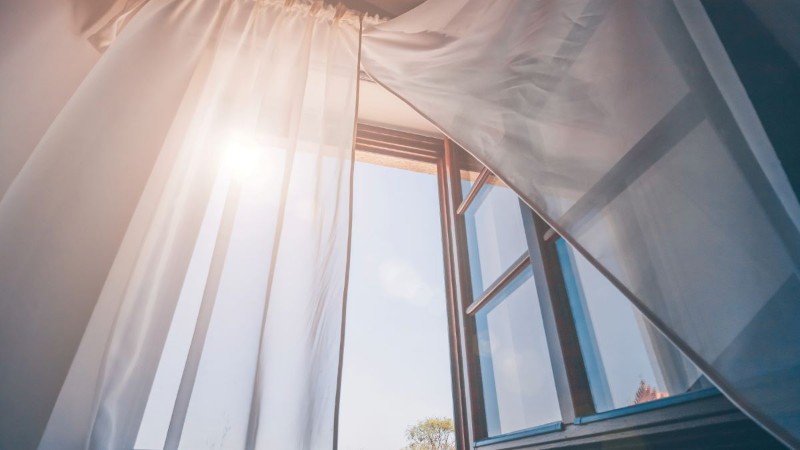 Sunlight streaming through an open window with white sheer curtains, creating a fresh and airy atmosphere in a room.