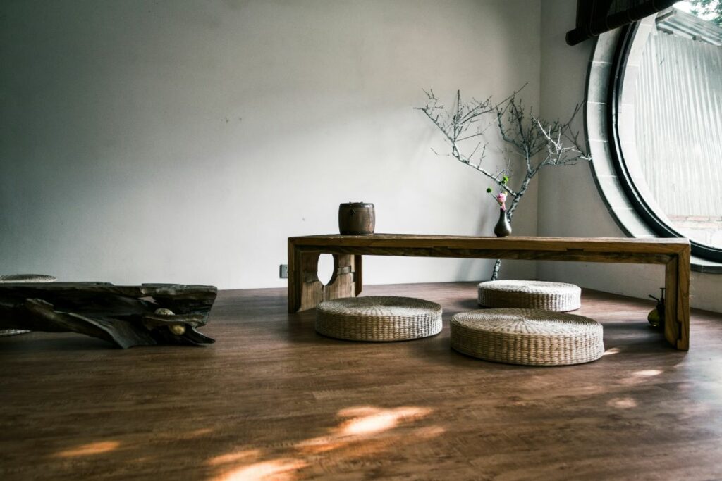 A minimalist, Japanese-inspired minimalism interior with a low wooden table and round floor cushions on a dark floor.
