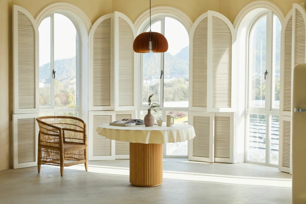 A stylish dining area in a sunroom with an arched window, a round table, and rattan chairs.