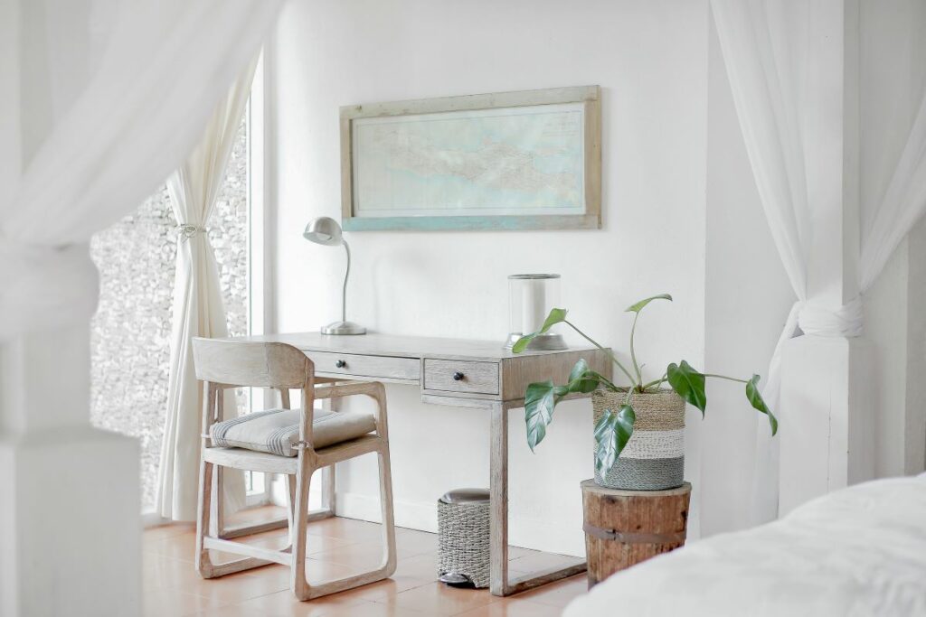A bright and airy minimalistic home office with a white desk, a simple wooden chair, and several potted plants.