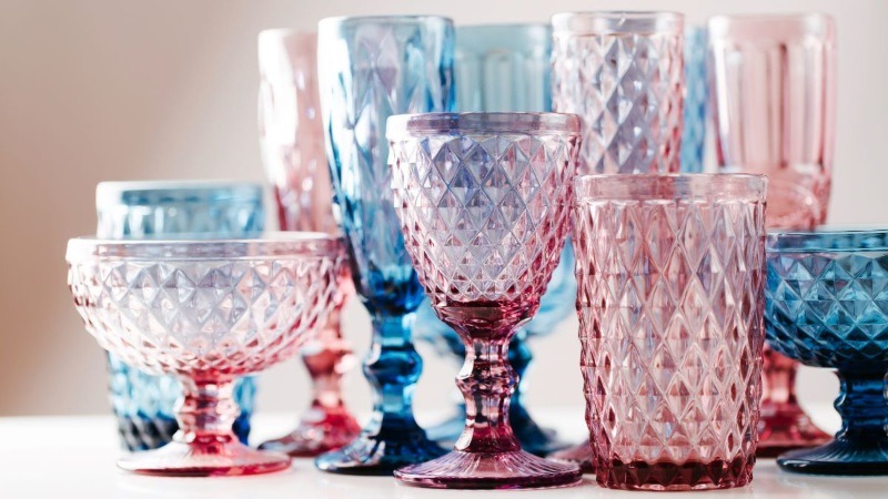 A collection of elegant, vintage-style drinking glasses in shades of pink and blue with a textured diamond pattern.