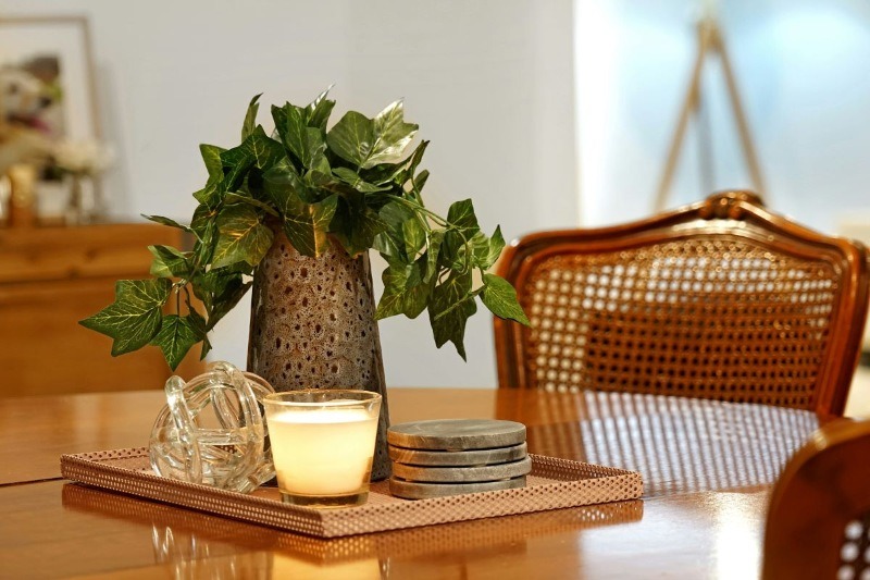 A close-up of a decorated wooden table featuring a lit candle on a tray, coasters, and a green plant in a stylish vase.
