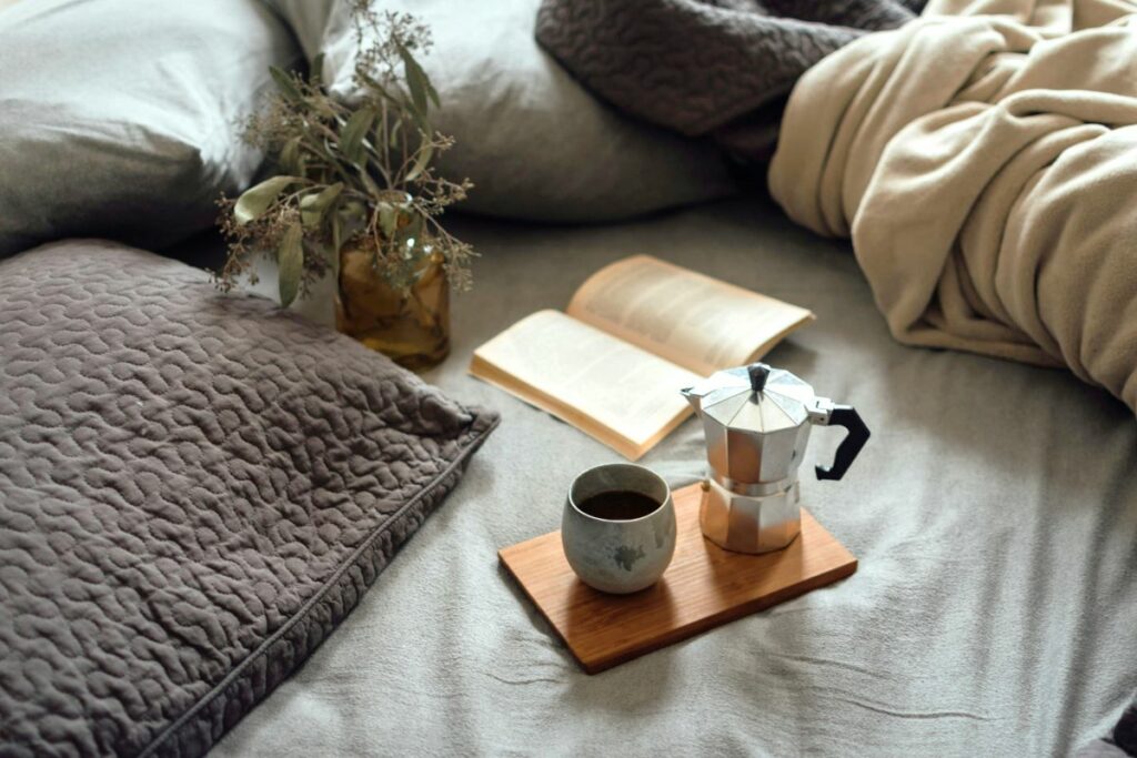 Minimalist lifestyle, a cozy bed scene with a coffee tray holding an open book and a moka pot, representing a relaxing morning.