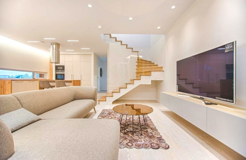 Minimalism interior design in a spacious and modern open-plan living room with a large L-shaped sofa and a floating wooden staircase.