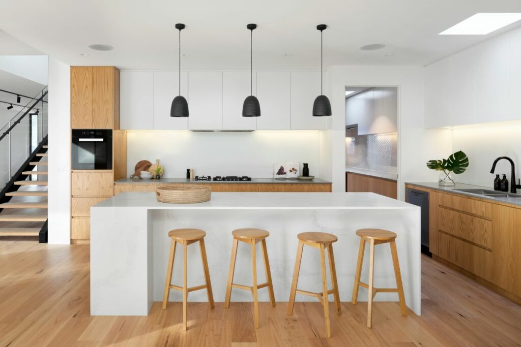 A modern minimalist interior design in the kitchen with a large white island, wooden bar stools, and black pendant lights.
