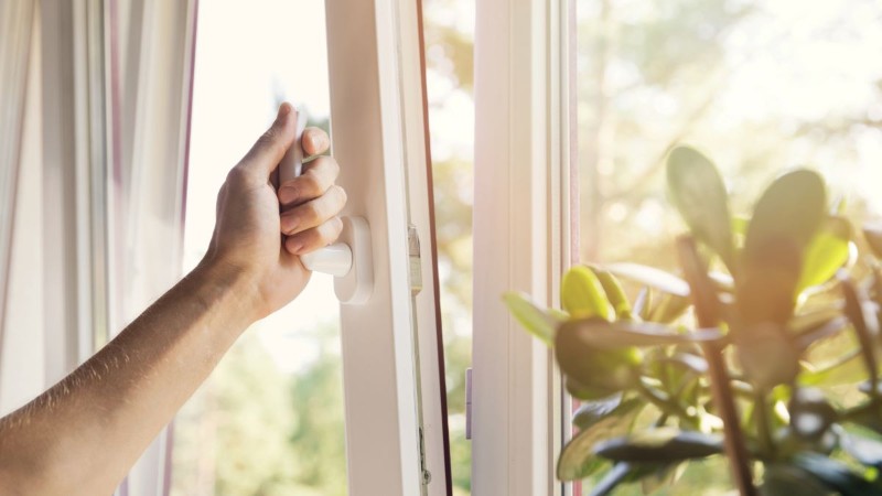 A person opening a window to let in fresh air and sunlight, a natural way to make your home smell clean and amazing.