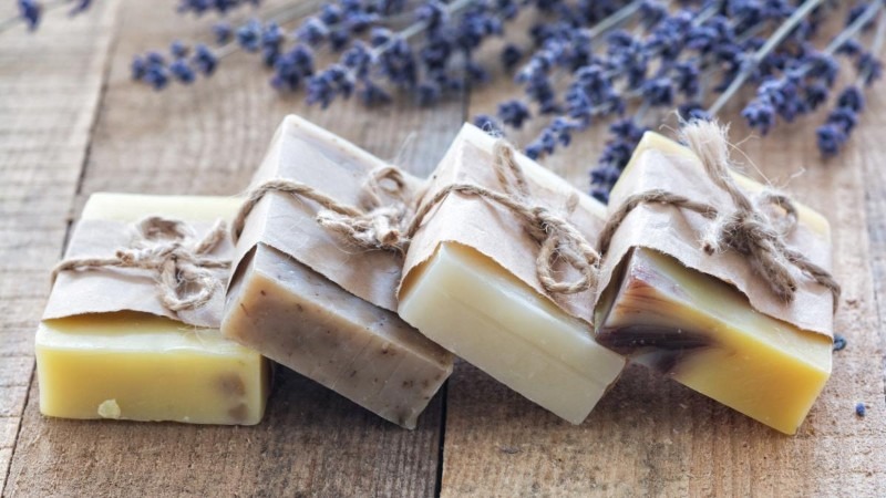 Several bars of artisanal, handmade lavender soap wrapped in paper and twine on a rustic wooden surface.