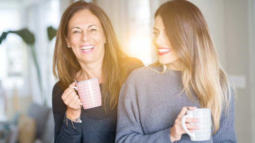 A mother and her adult daughter enjoying a warm drink together, smiling and sharing a happy moment.