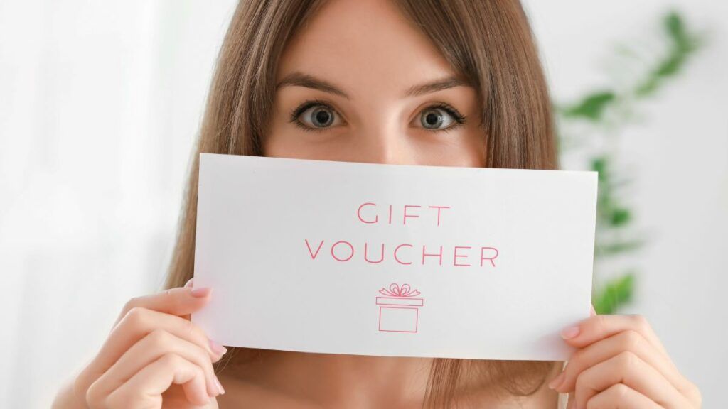 A woman holding up a gift voucher, with only her smiling eyes visible above it.