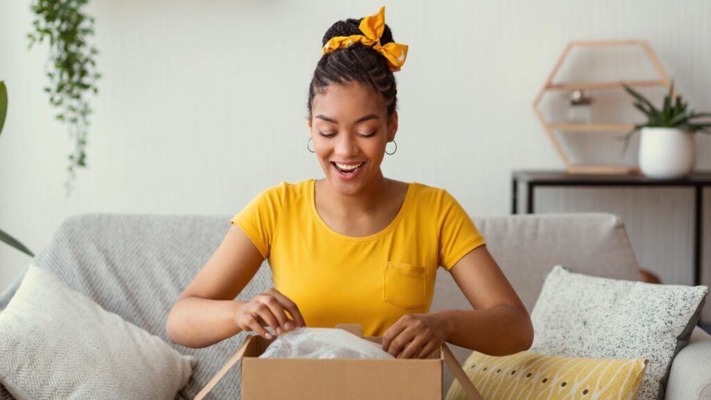 An excited young woman in a yellow shirt smiling as she opens a gift for minimalist.