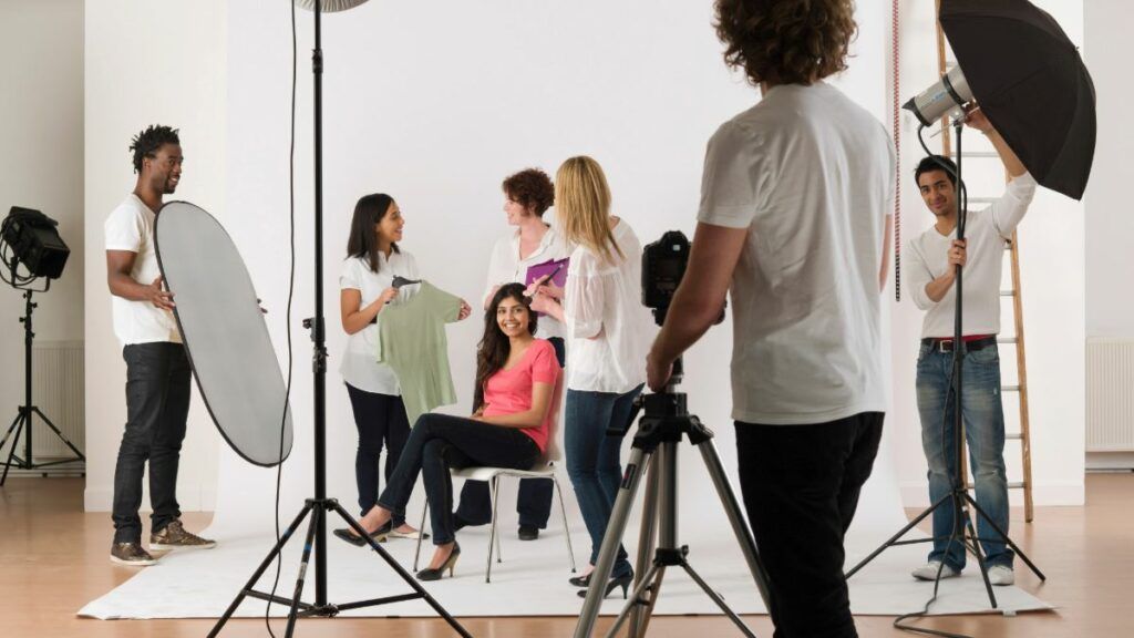 A behind-the-scenes view of a professional photoshoot, with a model posing and a crew operating cameras and lights.