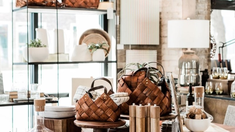 A chic home decor display featuring a woven brown leather tote bag and other curated items on a glass shelf.