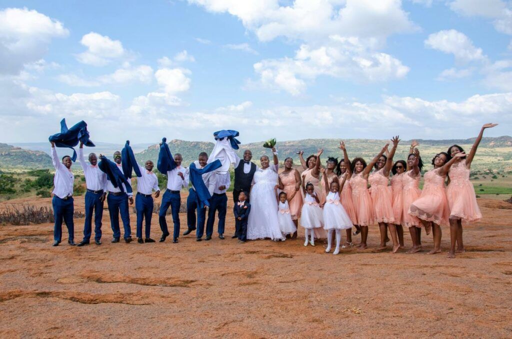 An African wedding party posing for a photo outdoors, with the groomsmen and bridesmaids in coordinated attire celebrating the couple.