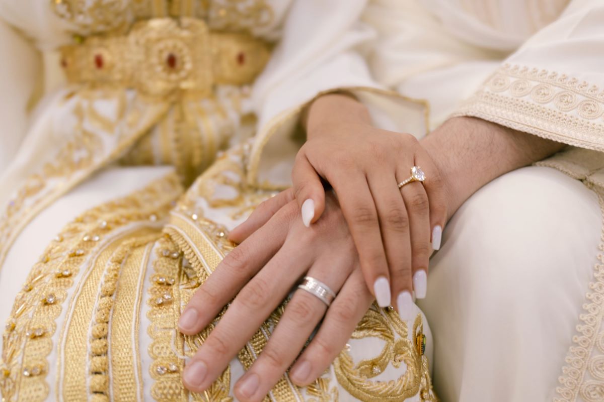 The hands of a Muslim bride and groom showing their wedding rings, resting over traditional embroidered wedding attire.