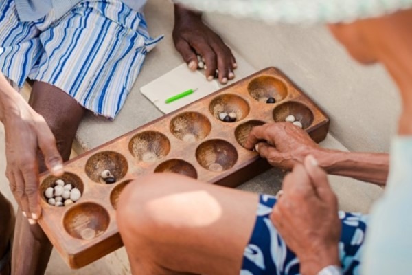 A close-up of a game of Mancala (or Congkak), a traditional count-and-capture board game popular as a social activity in Africa and Southeast Asia.