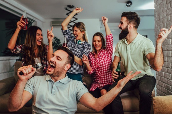 An energetic group of friends singing and cheering enthusiastically on a sofa, representing a lively karaoke night or house party theme.