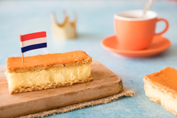 A traditional Dutch birthday treat, a 'tompouce' pastry, served with a small flag of the Netherlands and a celebratory paper crown in the background.