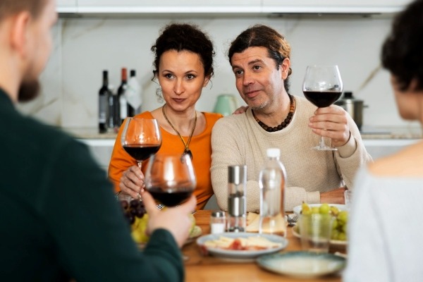 A couple at a dinner party representing the European tradition of 'Sobremesa,' toasting with red wine and enjoying conversation after a meal.