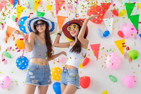 Two young women celebrating a birthday in Vietnam with confetti falling around them, representing a modern and joyful party tradition.