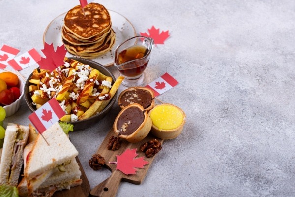 A display of iconic Canadian foods for a birthday celebration, including pancakes with maple syrup, poutine, and butter tarts, decorated with Canadian flags and maple leaves.
