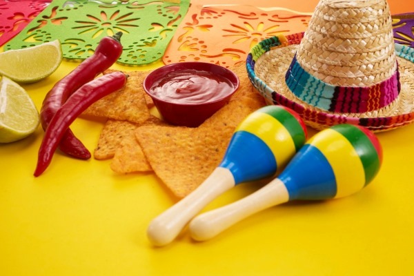 A festive flat lay representing a Mexican birthday fiesta, with tortilla chips, salsa, maracas, and a small sombrero on a bright yellow background.