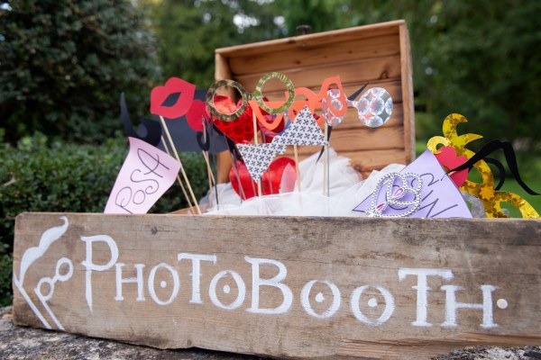 A rustic wooden crate labeled 'Photo Booth' filled with fun and silly props like glasses and lips, a creative party theme idea for guest entertainment.