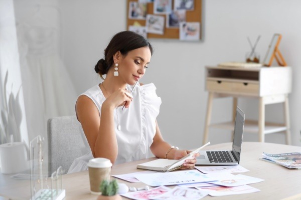 An organized woman at her desk engaged in the party planning process, using a laptop and notebook to organize a creative party.